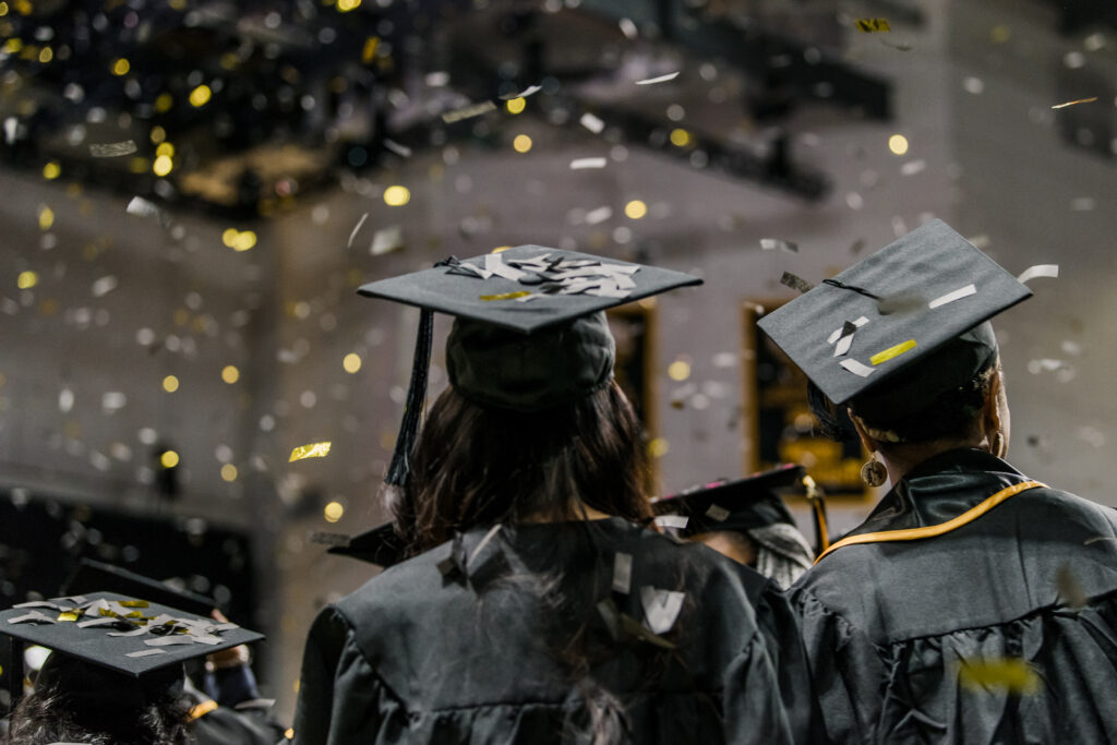 Two graduates in black caps and gowns, seen from the back, with confetti falling