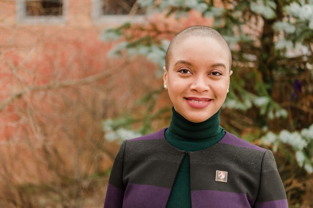 Portrait of a black woman in a striped blazer and turtleneck shirt, wearing pin that reads 