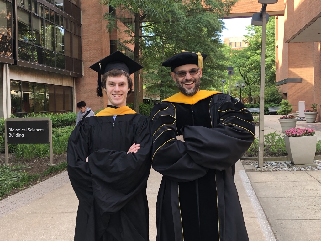 Nathan Myers and Sebastian Deffner in graduation robes, grinning, on UMBC's Academic Row.