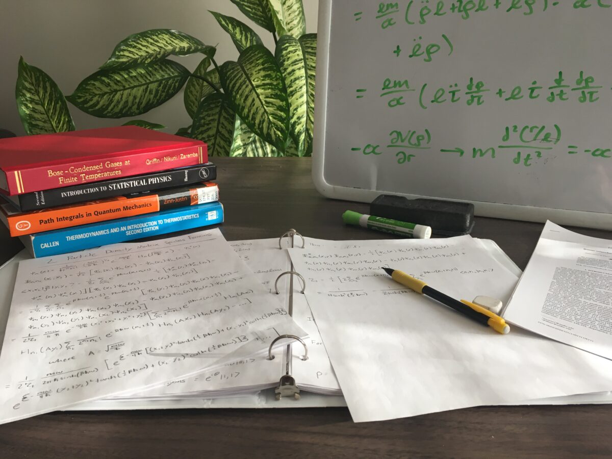 a pile of books and papers and a white board covered in handwritten equations