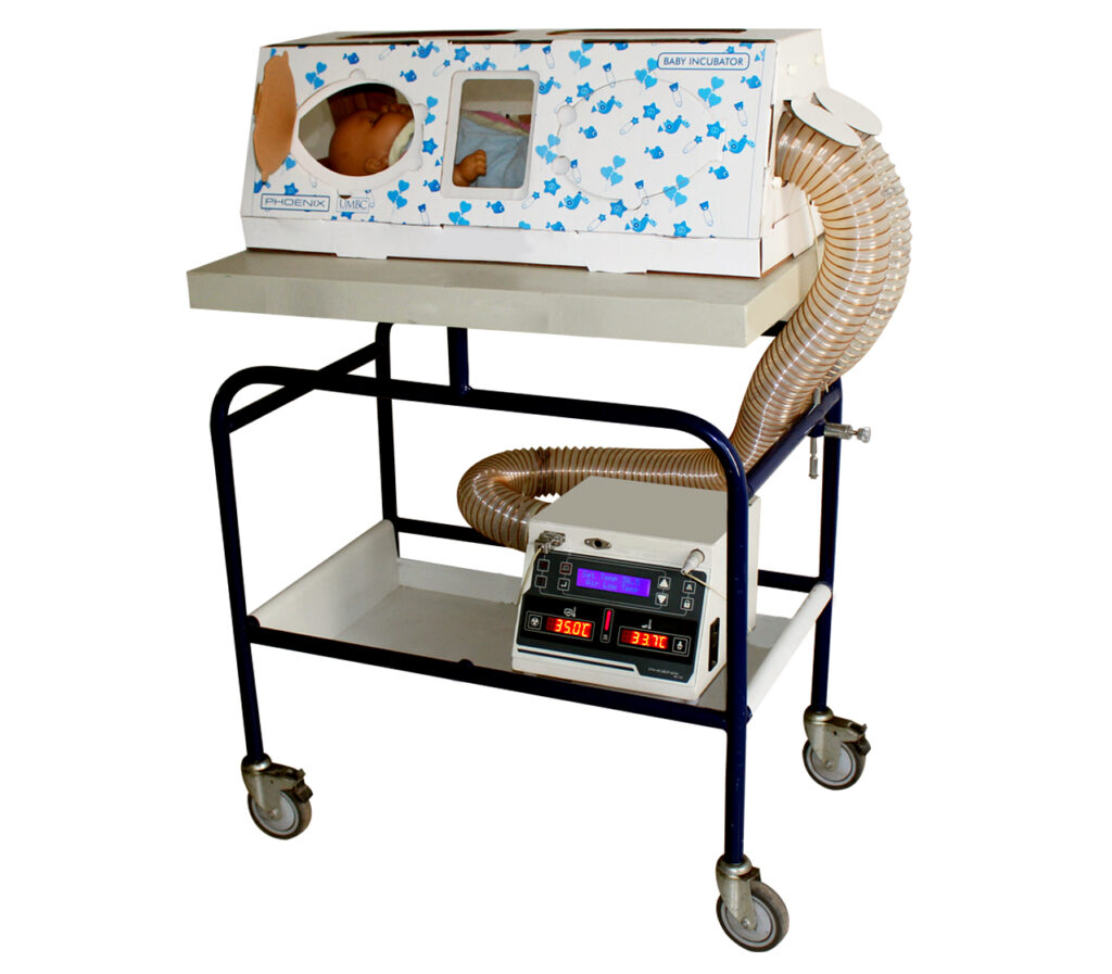 A black and white rectangular push cart with two levels carries a card board box with small blue flowers on the front of the box. Inside the box is a baby doll. A plastic ribbed tube is inserted into the end of the box that connects to a digital medical monitor box beneath. 