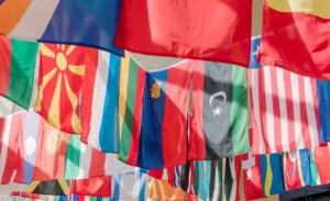 Flags from nations around the world hanging in the air, brightly lit by natural light from a window