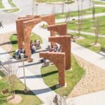 A large outdoor sculpture made of orange colored cement shaped in eight consecutive arches