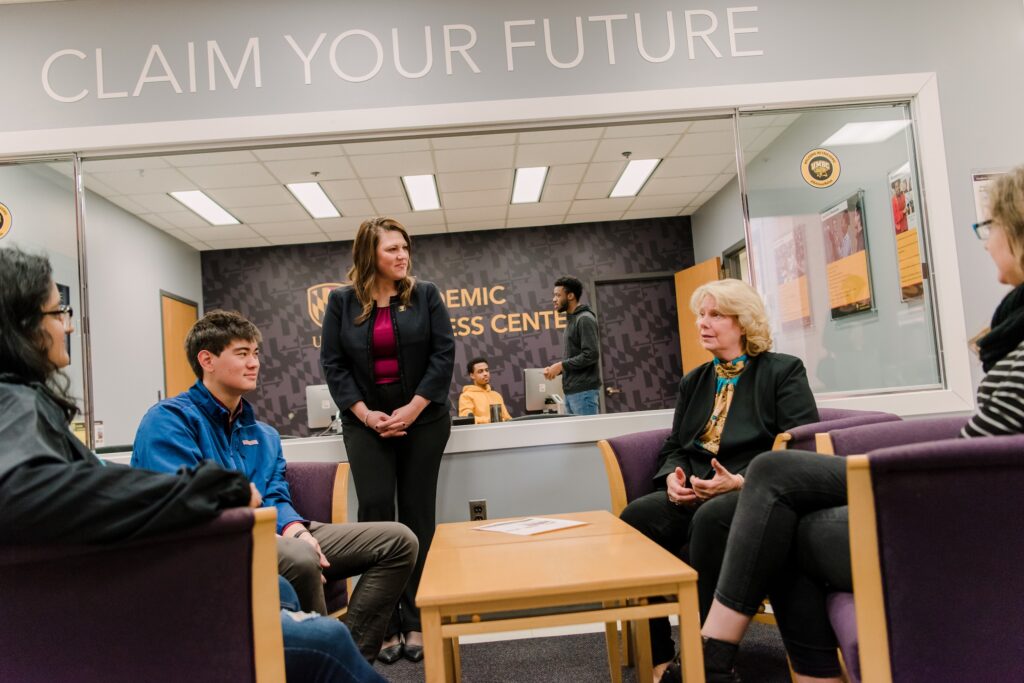 A group of people talks around a table. A sign above them reads 