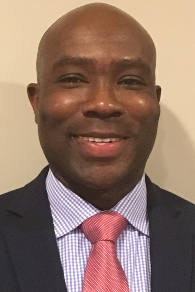 Portrait of smiling middle-aged Black man in suit, striped shirt, and pink tie.