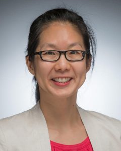 Headshot of woman wearing glasses, cream blazer and pink shirt