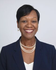Professional portrait of a middle-aged black woman with short hair. She is smiling and wears a navy blazer and three strands of pearls.