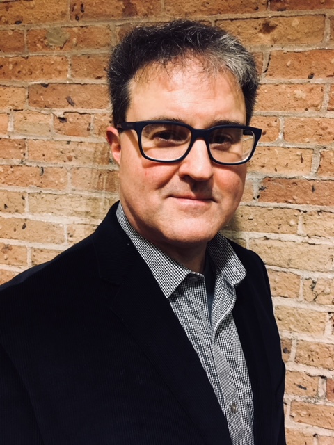 a headshot of a man with glasses and a suit jacket on