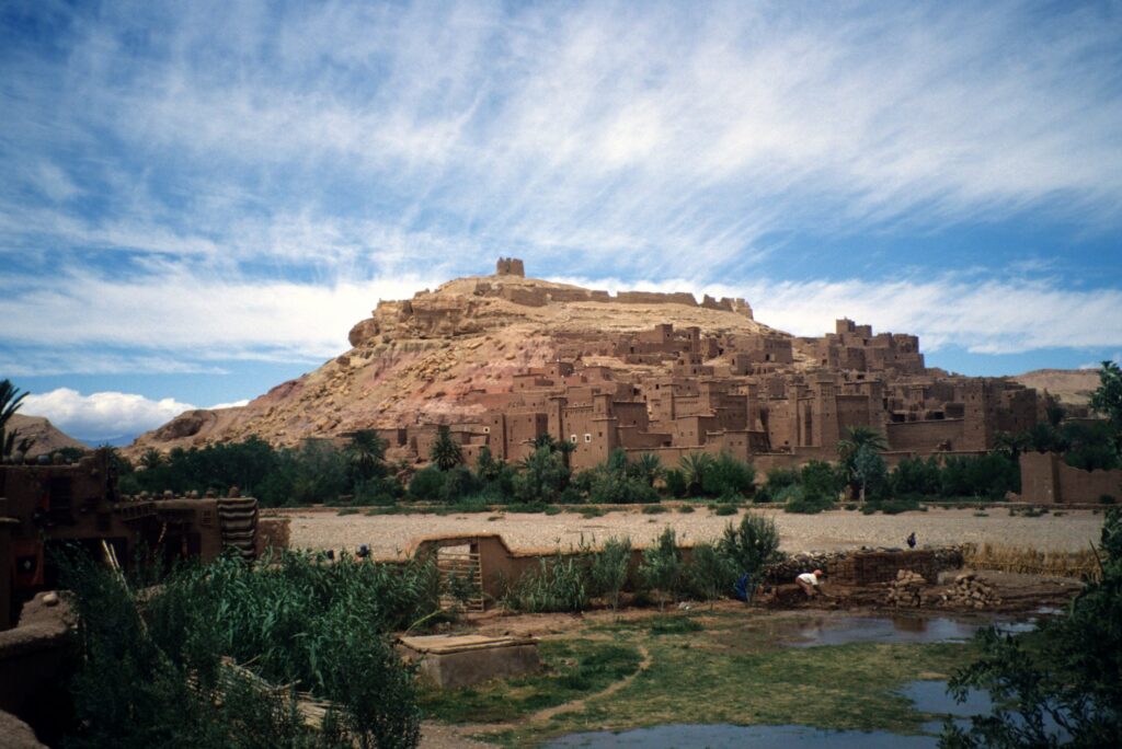 A group of ancient buildings made of light brown mud bricks on the side of a hill in Morocco.