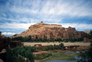 A group of ancient buildings made of light brown mud bricks on the side of a hill in Morocco.