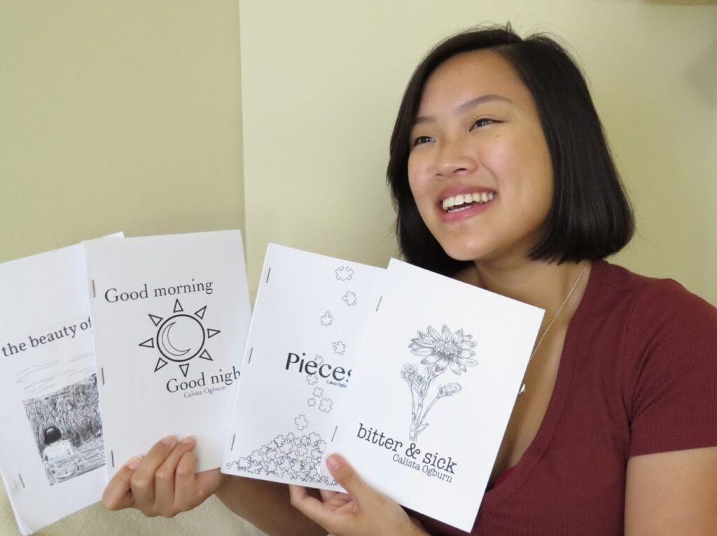 Young Asian woman holds up four small books. She smiles as she shows their covers.