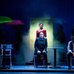 Student actors stand on a darkly lit stage