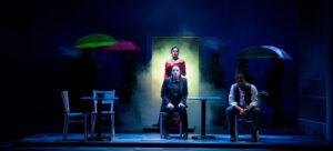 Student actors stand on a darkly lit stage