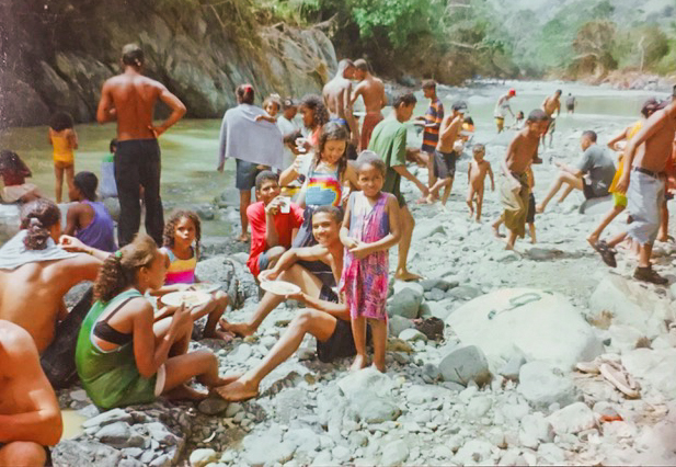 A large group of adults and children swim in a river on a sunny day. 