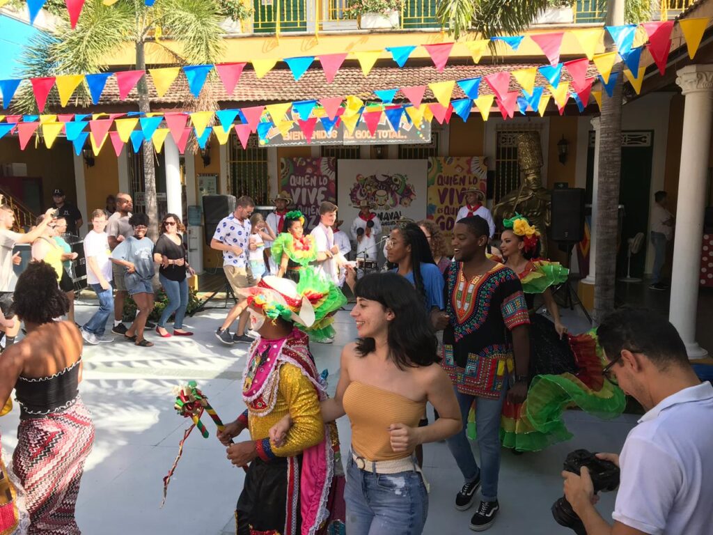 A group of people wearing brightly colored clothes dance in a circle in an outdoor plaza.