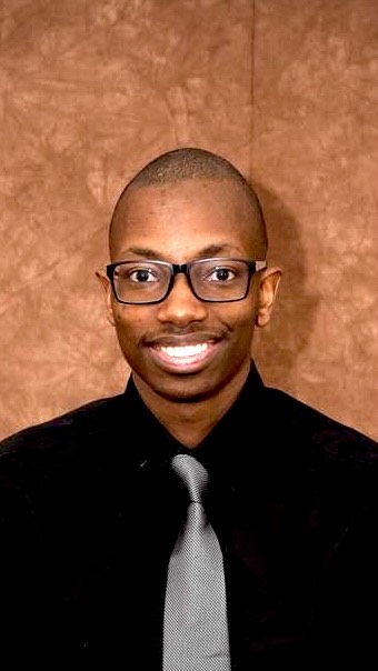 Portrait of a young man wearing glasses, a black dress shirt, and tie.