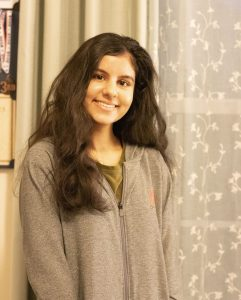 A woman with long brown hair smiles. She is wearing a grey shirt. 