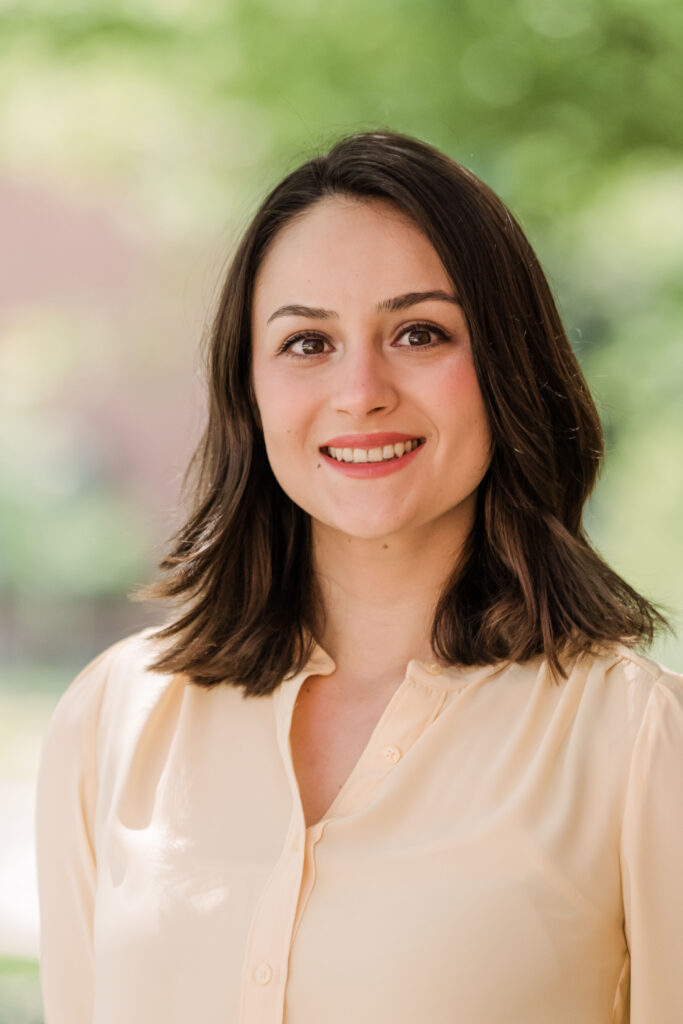 Portrait of a young woman with shoulder-length brown hair. She wears a dress shirt.