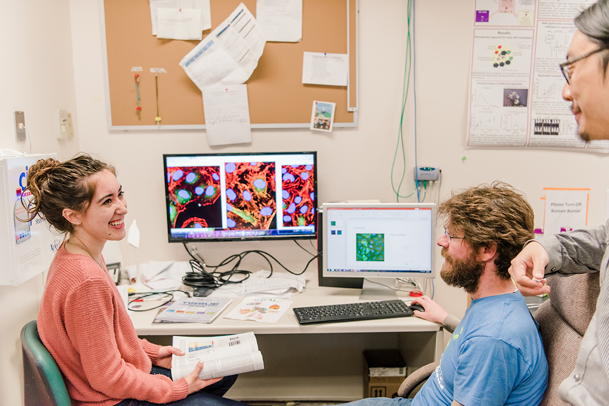 two students looking at microscope imagery on a computer, overlooked by their instructor
