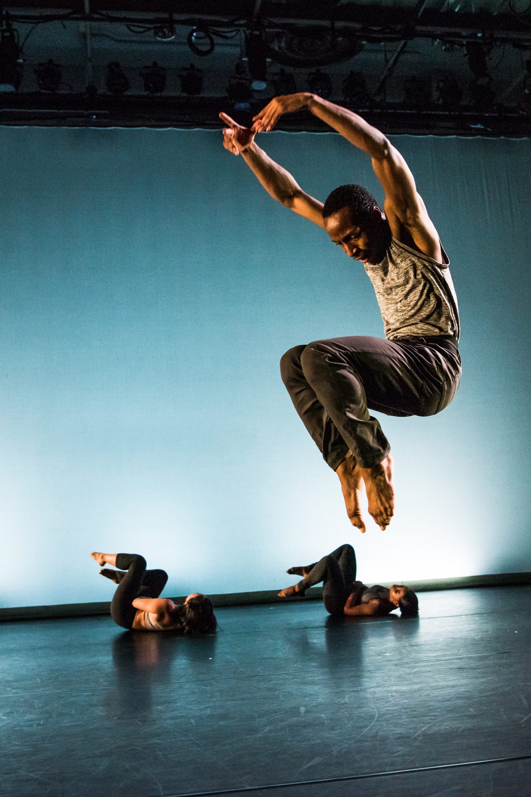 one dance student jumping in the air with two posing below
