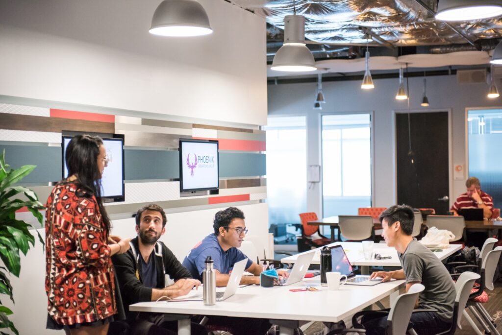 Students sitting at a table together having a discussion, while someone oversees them.