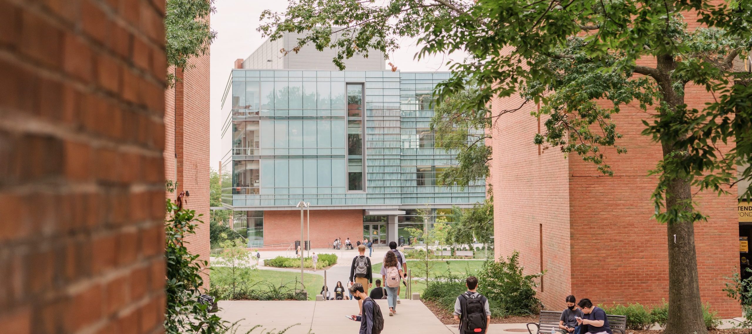 Students walking across a university, with large brick and glass building in the distance.