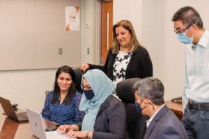 The iHARP research team sitting and Vandana Janeja standing. All are looking at a laptop screen