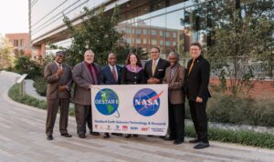 group of seven people outdoors holding a large banner in front of them with the NASA logo