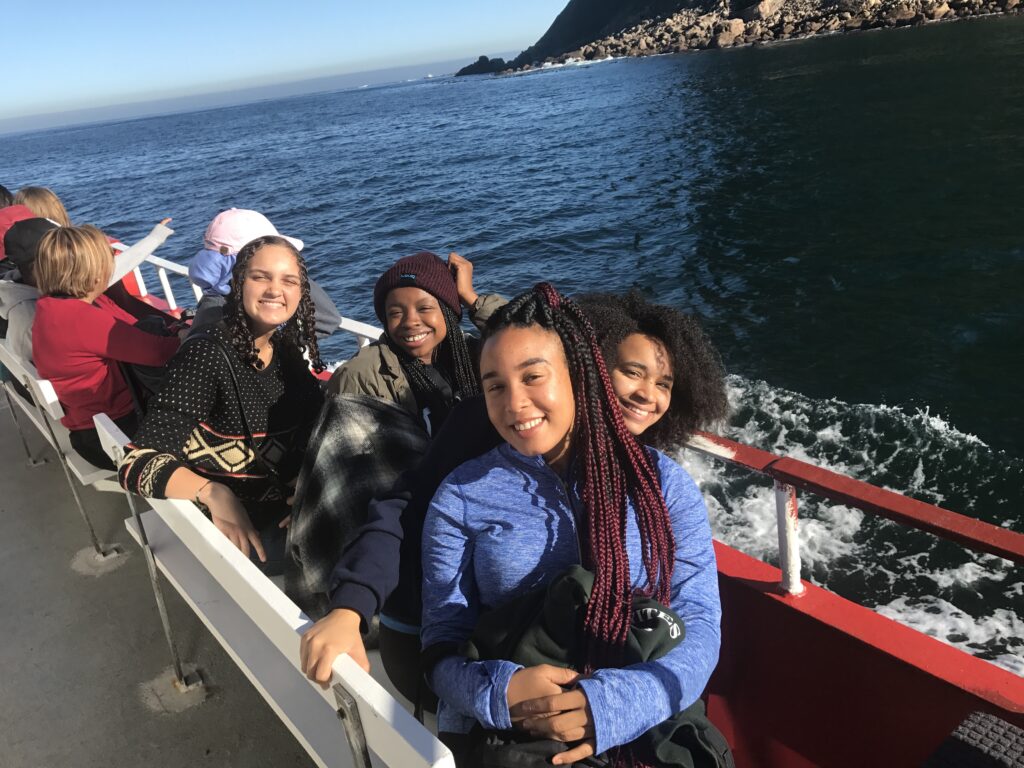 A group of women sit outside on benches on the deck of a boat out in the ocean.