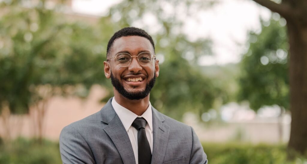 A man wearing glasses smiles at the camera.