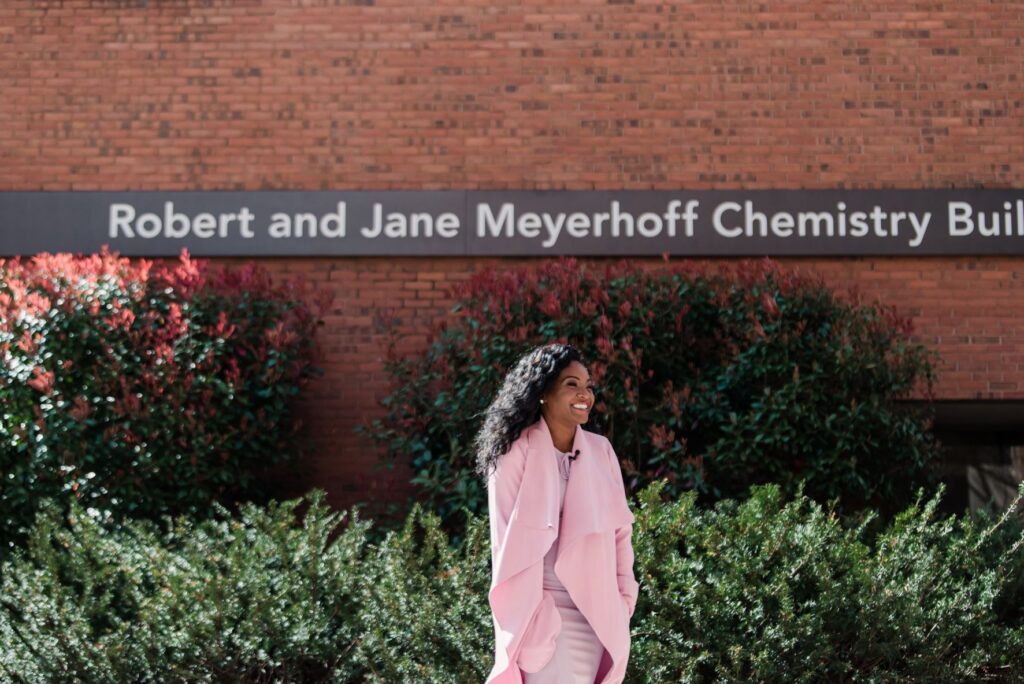 Woman in lilac professional outfit walks through a courtyard. Text behind her reads 