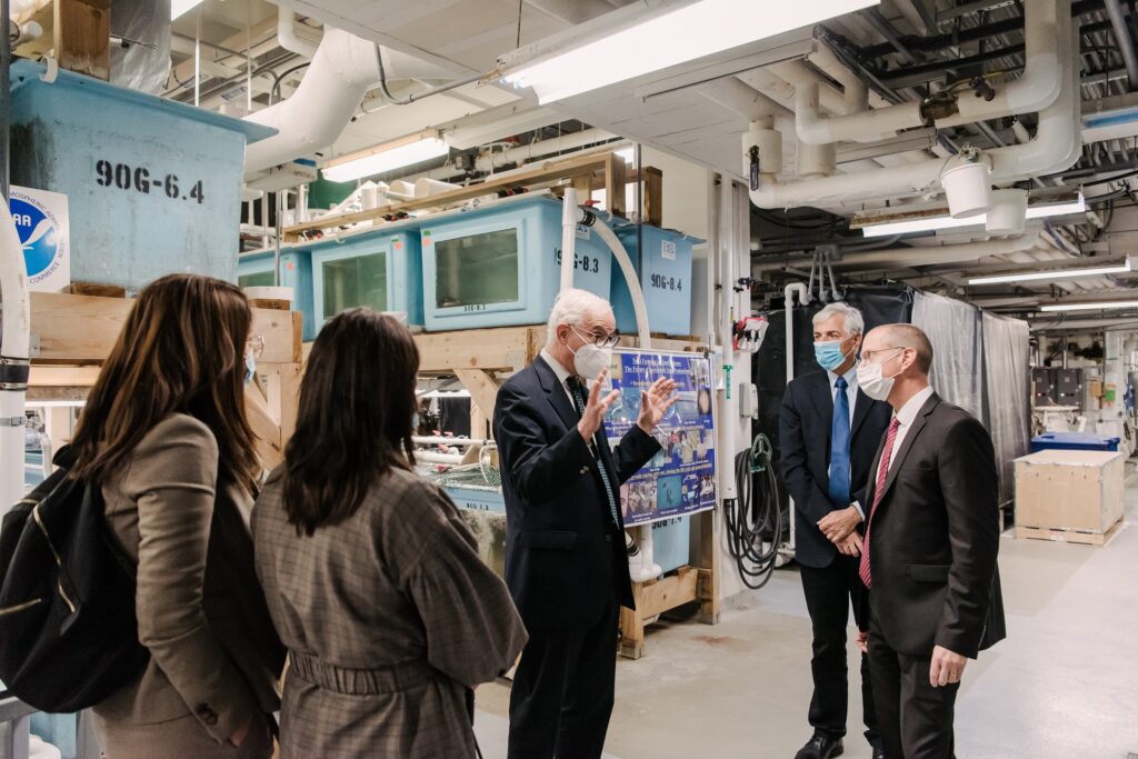 five people in business attire in an industrial-looking basement, one speaking 