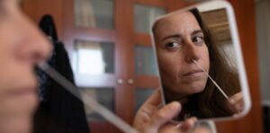 woman tests herself for corona virus in a small mirror|UMBC COVID-19 test pop up|