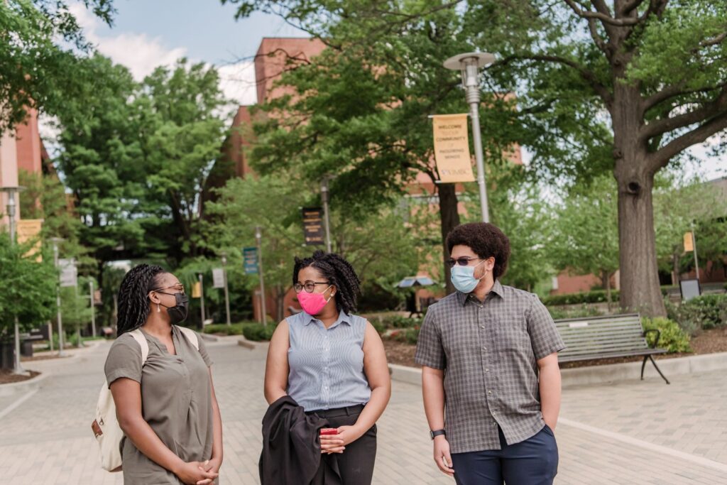 Three students walk down a path at a university campus in spring
