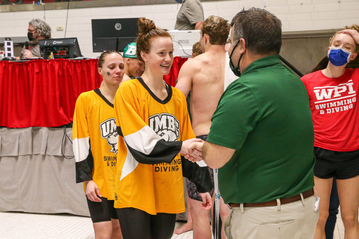 Women wearing a UMBC swimming and diving shirt shaking hands with a man in a green polo shirt