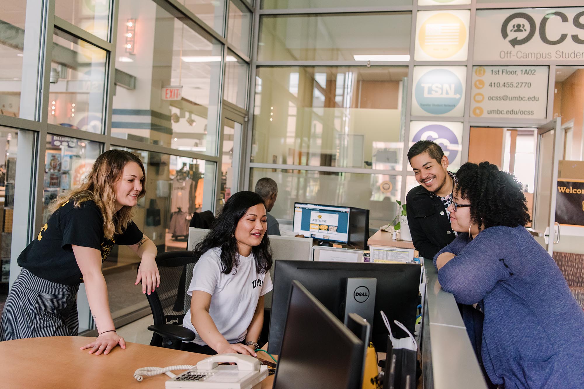 Students of varying genders and ethnicities gather around for an engaging brainstorming session. One young woman is on the computer, while others surround her.