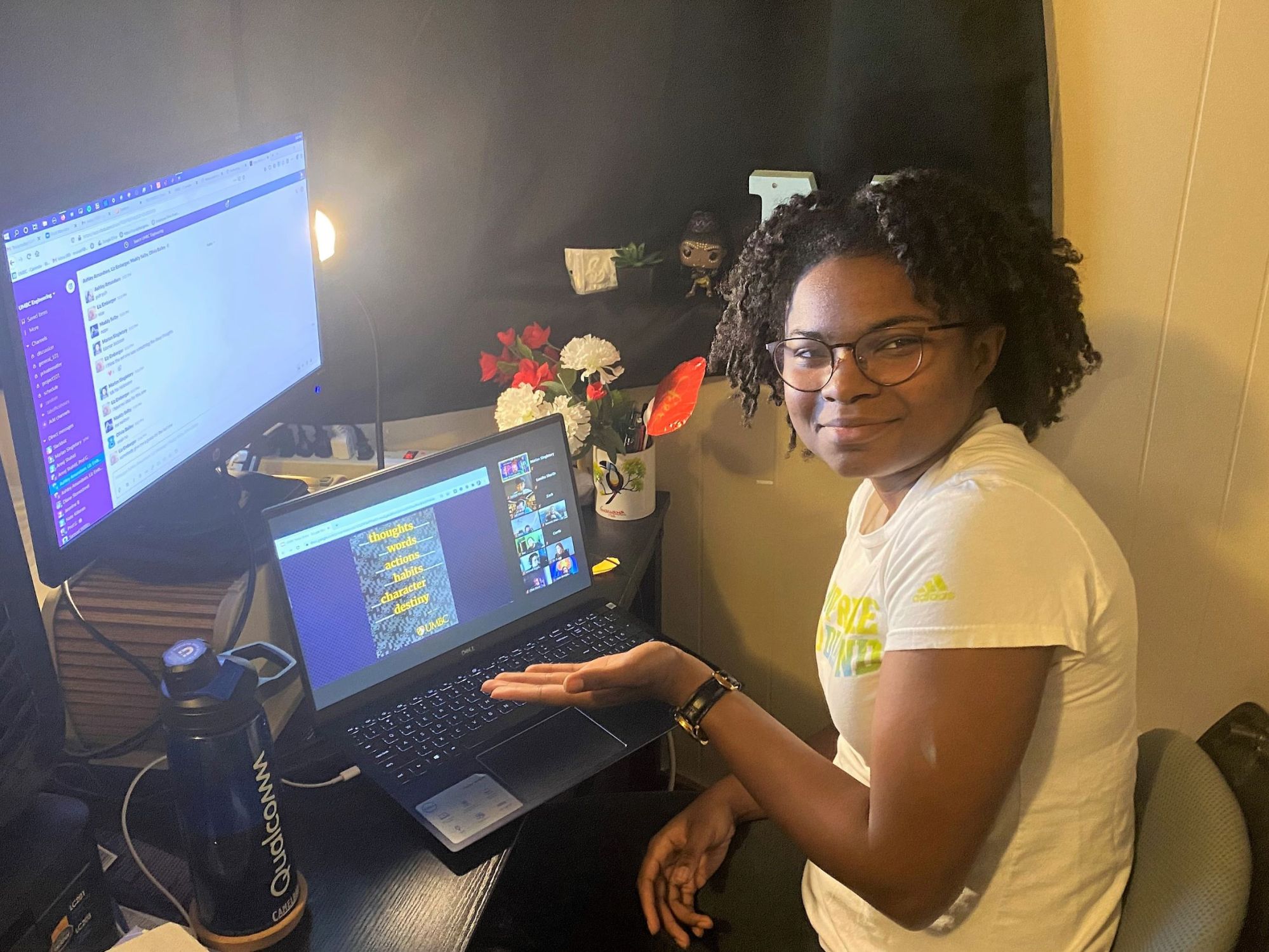 Young black woman with wire-frame glasses smiles into the camera, showing two computer screens.