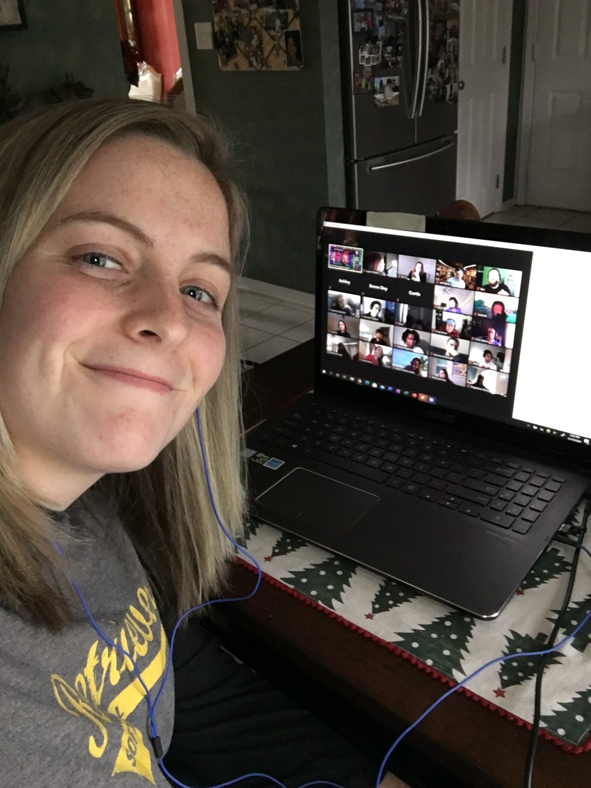 Young smiling young woman with blonde hair and wearing a Retrievers softball shirt poses with her loptop, featuring a screen of faces.