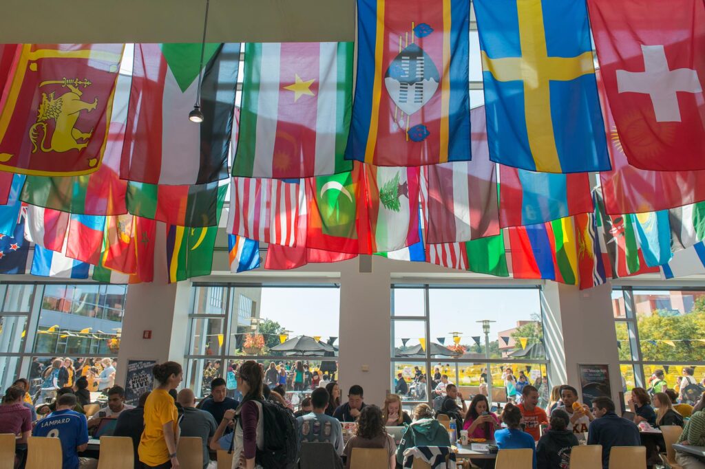 Flags from different countries from all around the world hang from the ceilings in UMBC's commons. Students and faculty gather underneath.