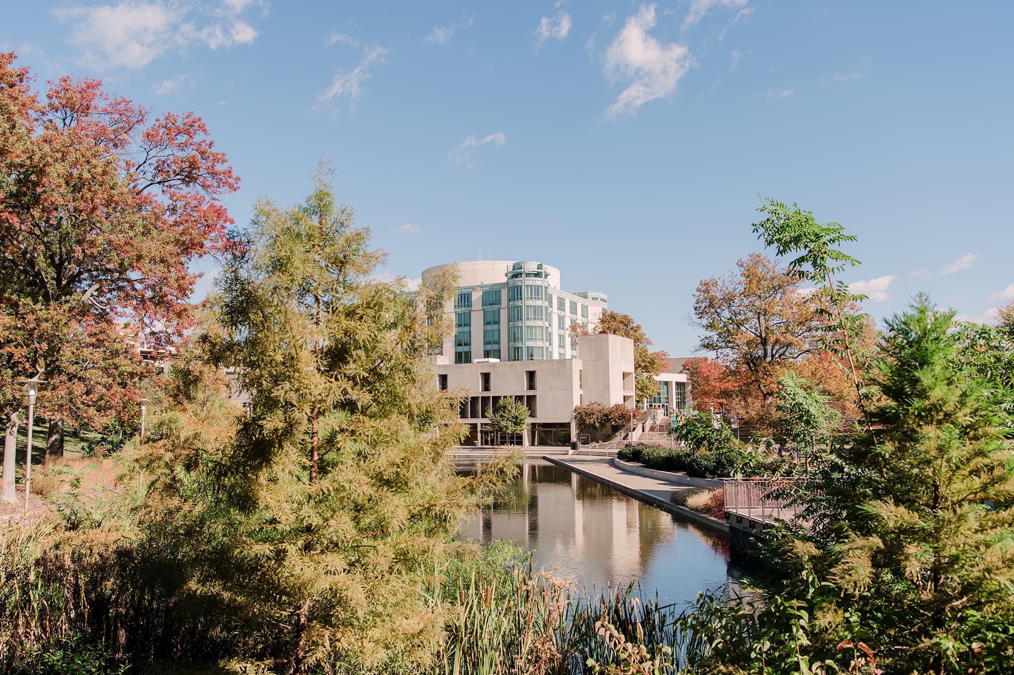UMBC's campus in the fall, featuring the AOK Library and its reflection in a pond surrounded by red, yellow, and green trees.