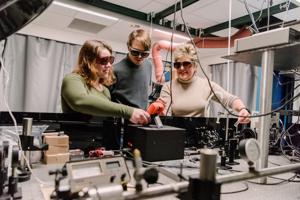 3 people working together in a technology lab, with protective eyewear on