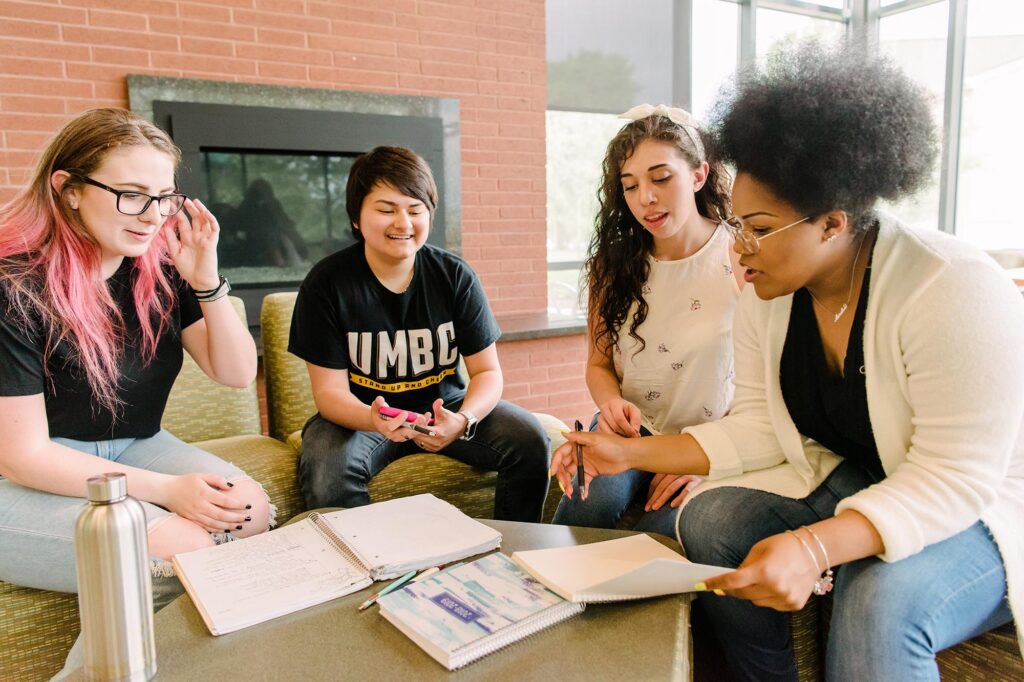 Four young adults sit around a table looking at notes. One wears a shirt reading, "UMBC".