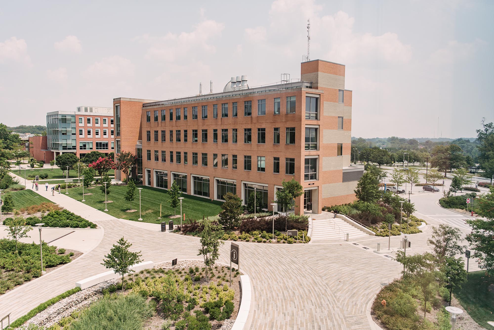 A perspective view of some of UMBC's well-known brick buildings, surrounded by lush trees, with a forested horizon in the distance.