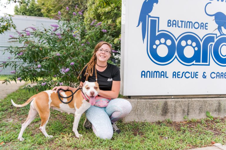 Laryssa posing with a dog next to a Baltimore animal rescue sign.