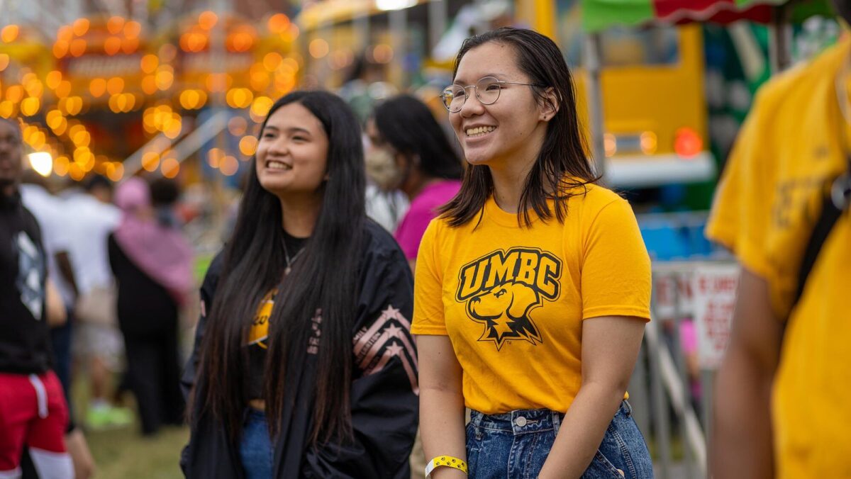 Two UMBC students attend an event. One wears a UMBC Retrievers shirt.