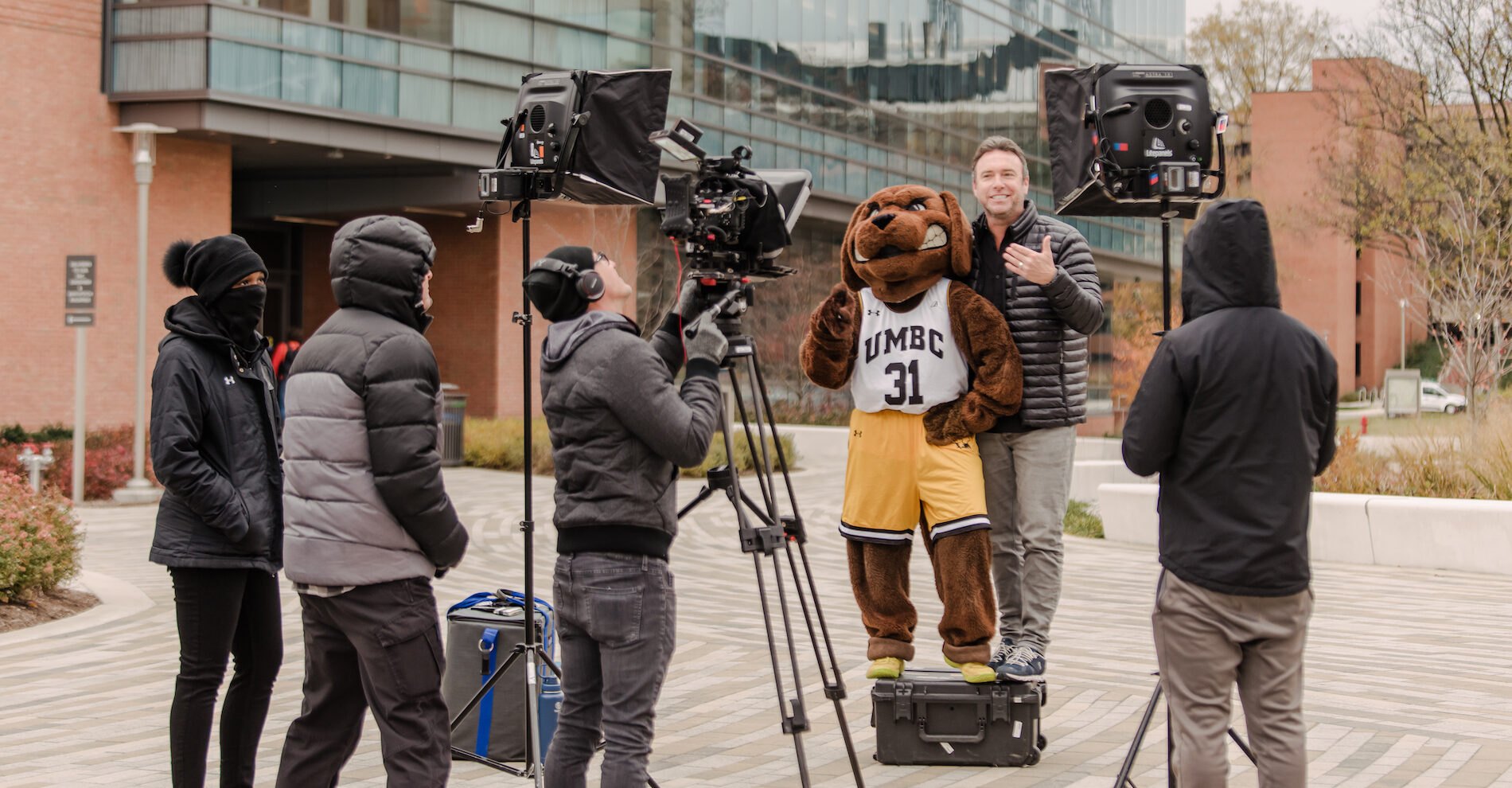 The College Tour host Alex Boylan poses in front of the camera with UMBC's mascot, True Grit in full retriever costume.