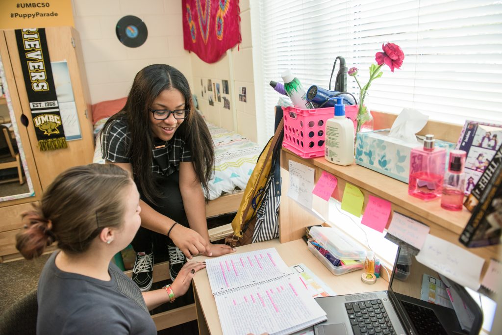 Two women are engaged in discussion over a desk, organized with a collection of pink items.