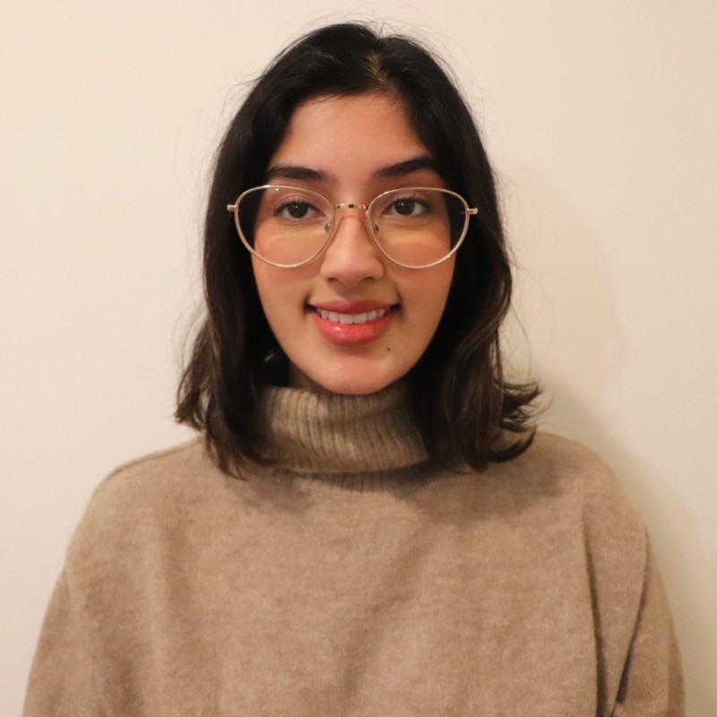 Headshot of smiling young woman wearing glasses and a sweater.