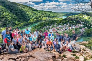 a large group on a rocky outcropping, backed by rolling green hills and a river