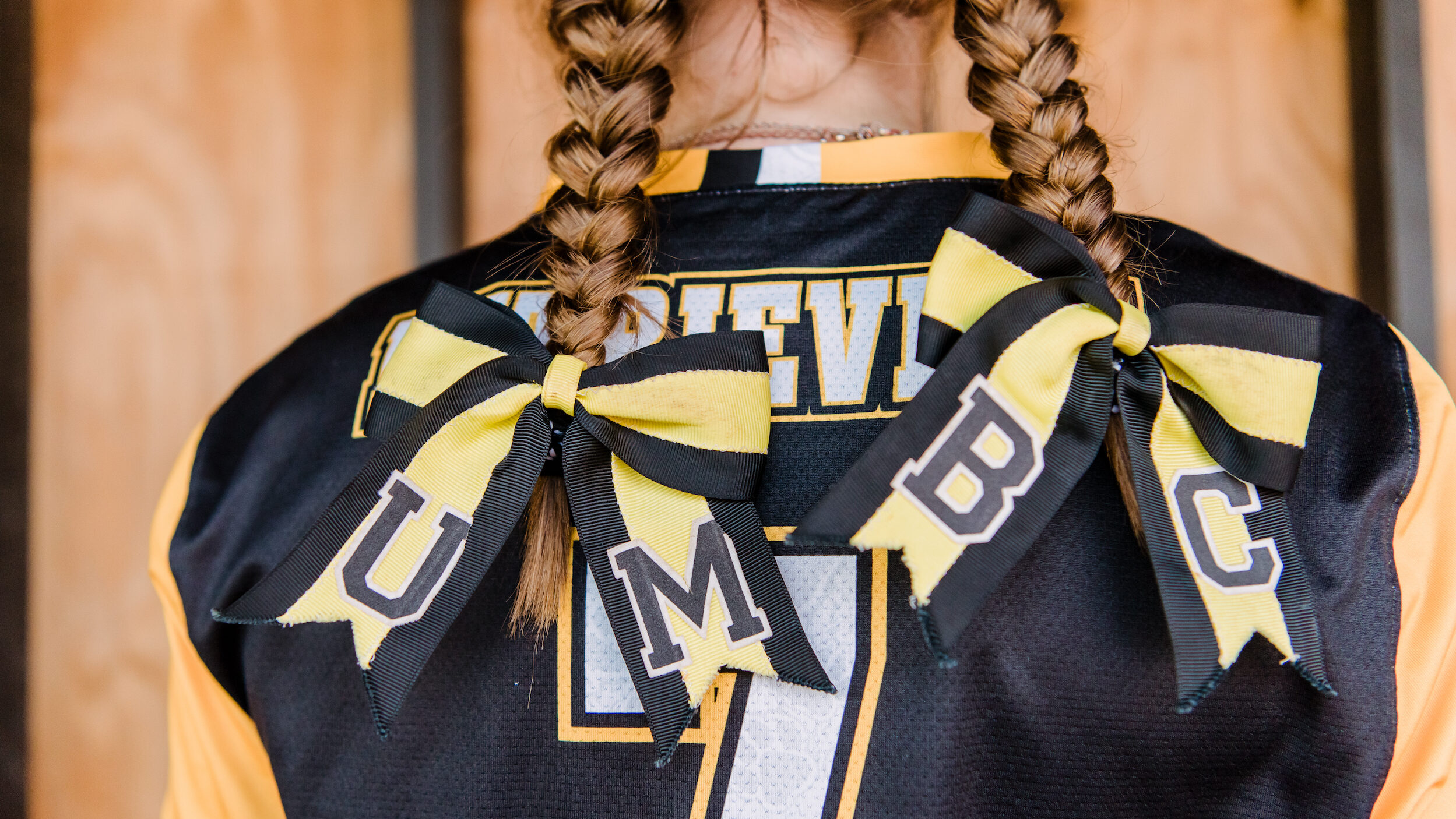 View of softball player's braided hair from behind with ribbons spelling "UMBC"